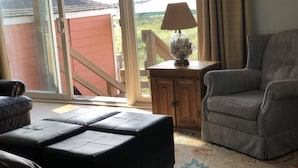 A living room with a sofa, ottoman, and a lamp on a wooden side table. - Oceanfront Duplex - Sleeps 10 - Great Price!! 3 B/R, 2.5 bath, outdoor shower (Atlantic Beach)