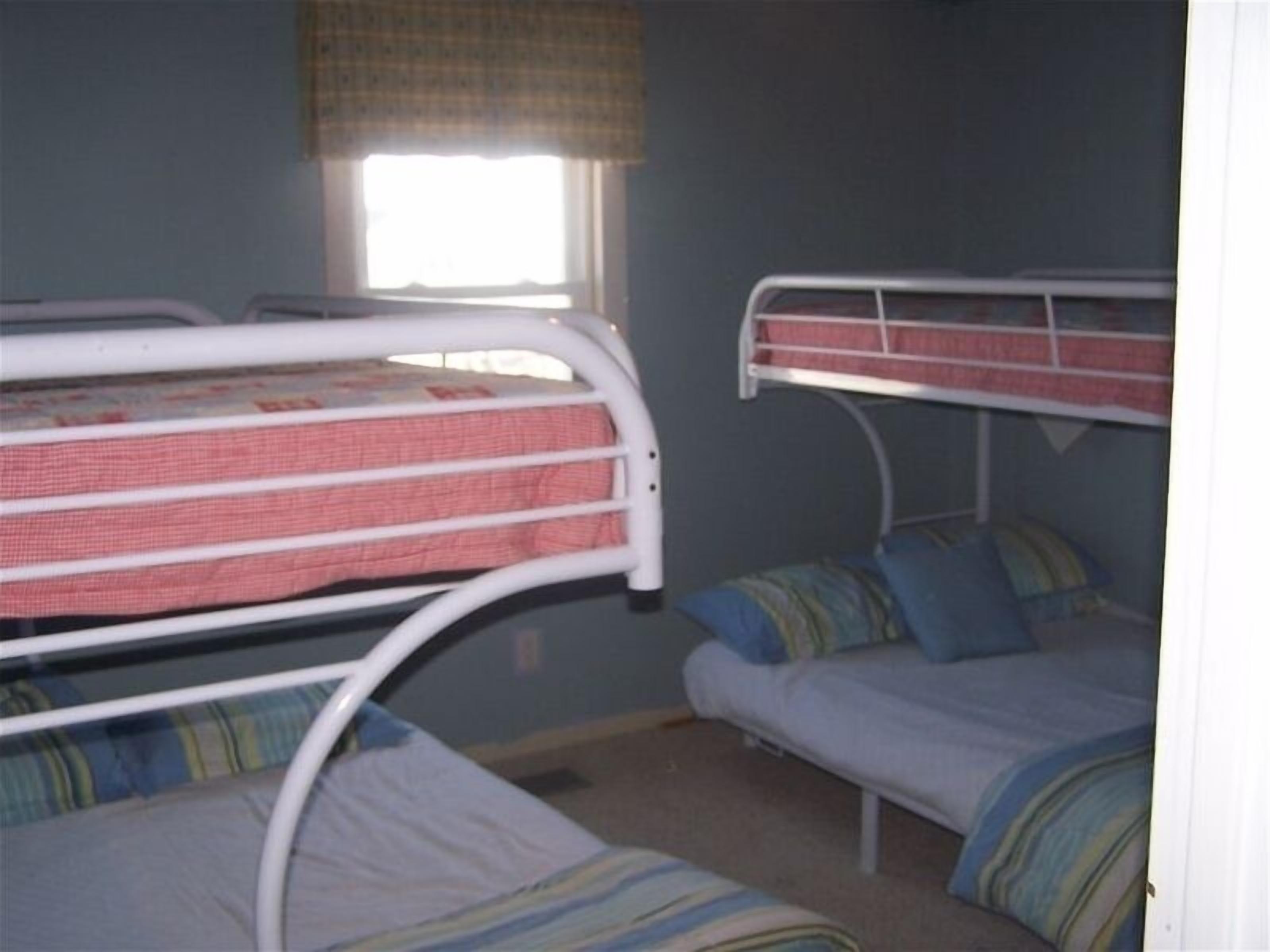 Ein Zimmer mit Etagenbetten, einem Fenster mit Vorhang und einer schlichten Wand.
