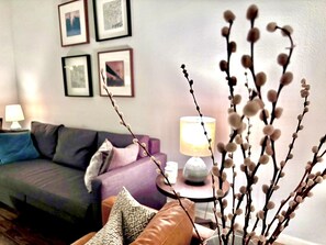 Un salon avec un canapé, des coussins, une lampe et des tableaux accrochés au mur.