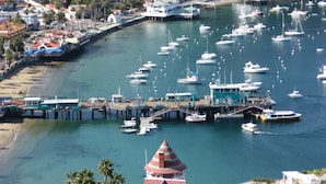 Un port de plaisance où sont amarrés de nombreux bateaux, une jetée qui le relie à la rive et un bâtiment imposant avec un toit rouge.