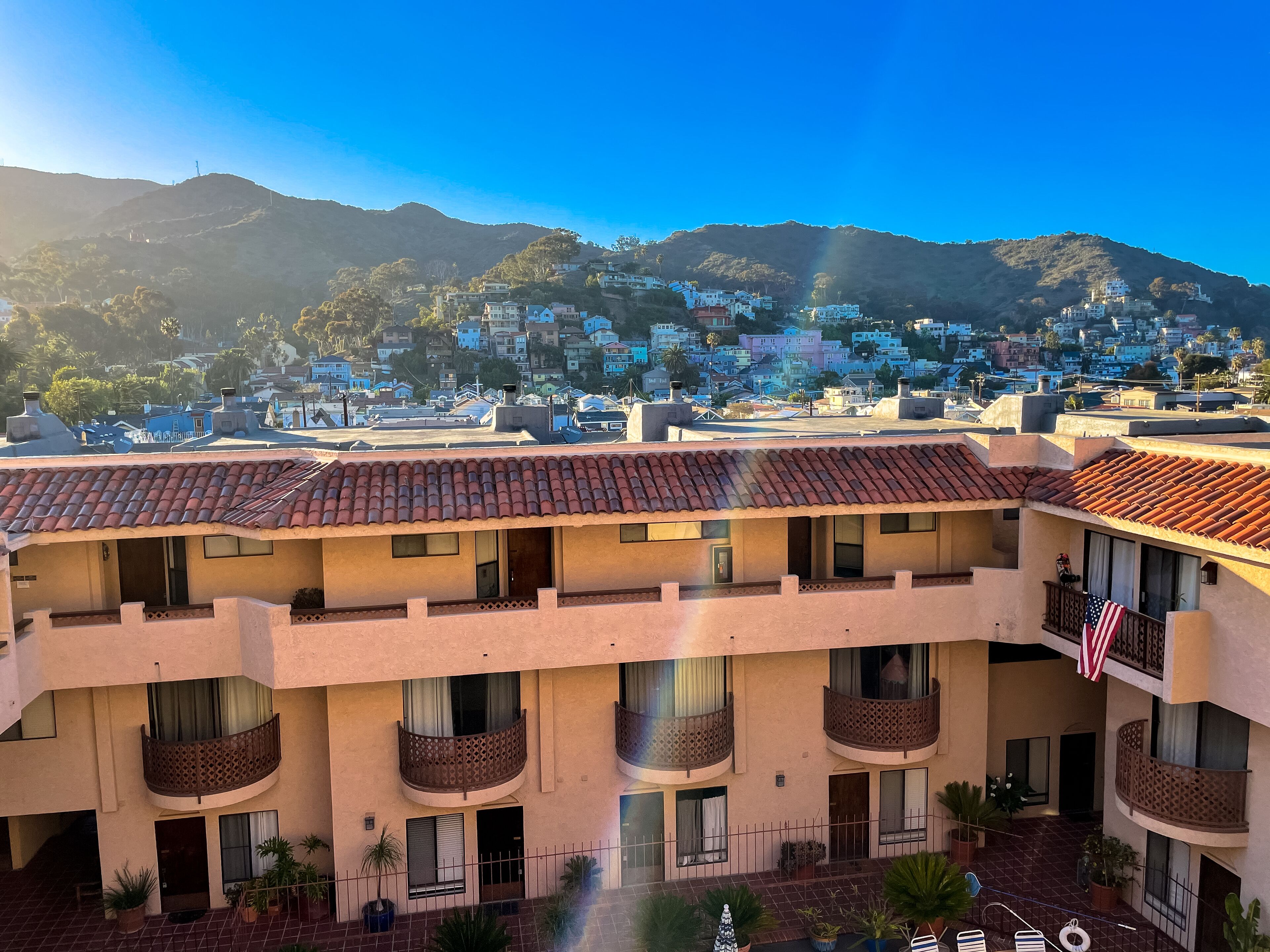 Un edificio de varios pisos con balcones, un patio interior y vistas a un pueblo en la ladera.