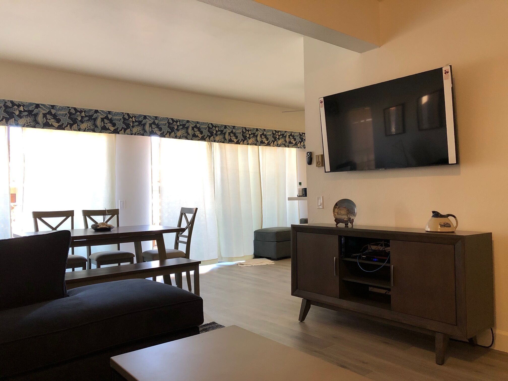 Un salon comprenant un canapé, une table basse, un téléviseur fixé au mur et un coin repas avec des chaises et une table.