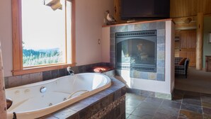 Un baño con una bañera grande, suelo de baldosas de piedra, ventana con vistas y una chimenea.