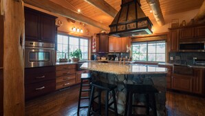 Una cocina amplia con armarios de madera, una isla grande con taburetes de bar, una pared decorativa de piedra y una lámpara colgante.