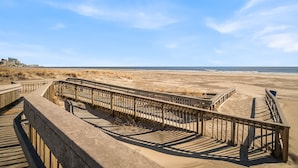 Un muelle de madera que conduce a una playa arenosa bajo un cielo despejado.