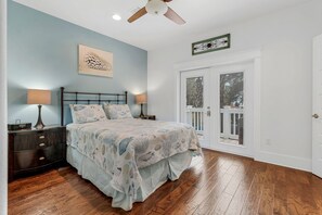 A bedroom with a bed, two bedside tables, a ceiling fan, a window with a view, and a door. - Nestled near beach-new updates-community pool-near shops, restaurants & cafes. (Santa Rosa Beach)