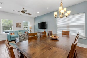 A dining room with a wooden table, chairs, a chandelier, a ceiling fan, and a television on the wall. - Nestled near beach-new updates-community pool-near shops, restaurants & cafes. (Santa Rosa Beach)