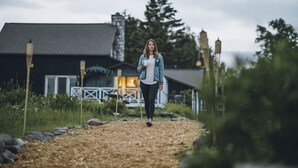 A person walking on a gravel path towards a building with a dark roof and white walls.