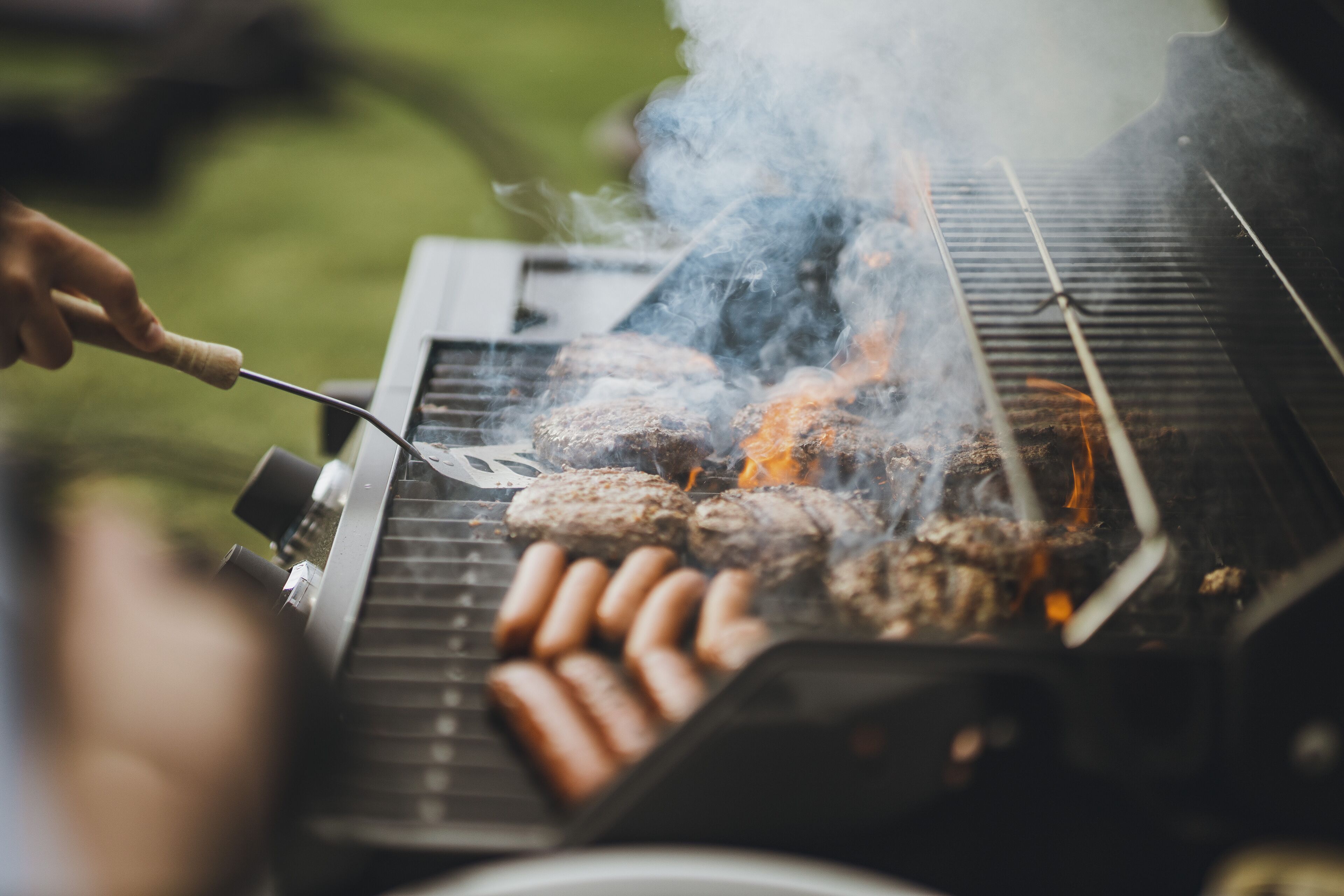 A grill with sausages and burgers being cooked.