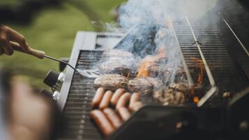 A grill with sausages and burgers being cooked.