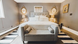 A bedroom with a large bed, two bedside tables with lamps, a sofa, and a striped rug.