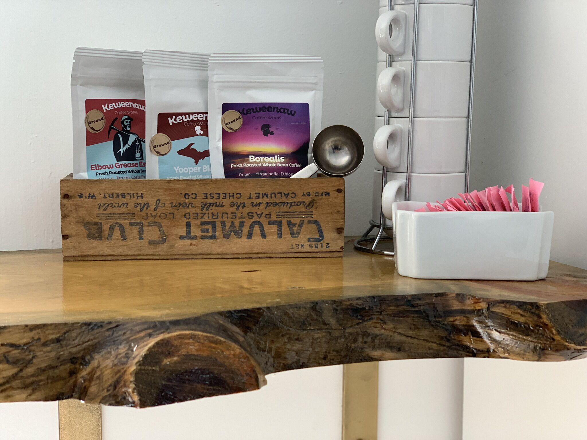 Eine Holzkiste mit dem Aufdruck 'ALAMYET', gefüllt mit Kaffeepackungen und einem Metall-Tassenhalter auf einer Holzoberfläche.