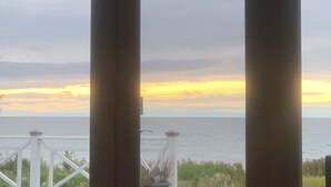 A view through large windows with a railing, overlooking a body of water and a sunset.