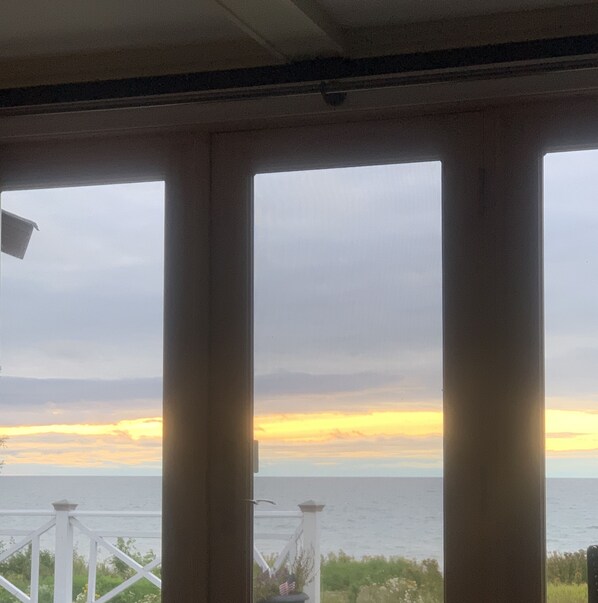 Vista a través de amplios ventanales con barandilla, sobre un cuerpo de agua y un atardecer.