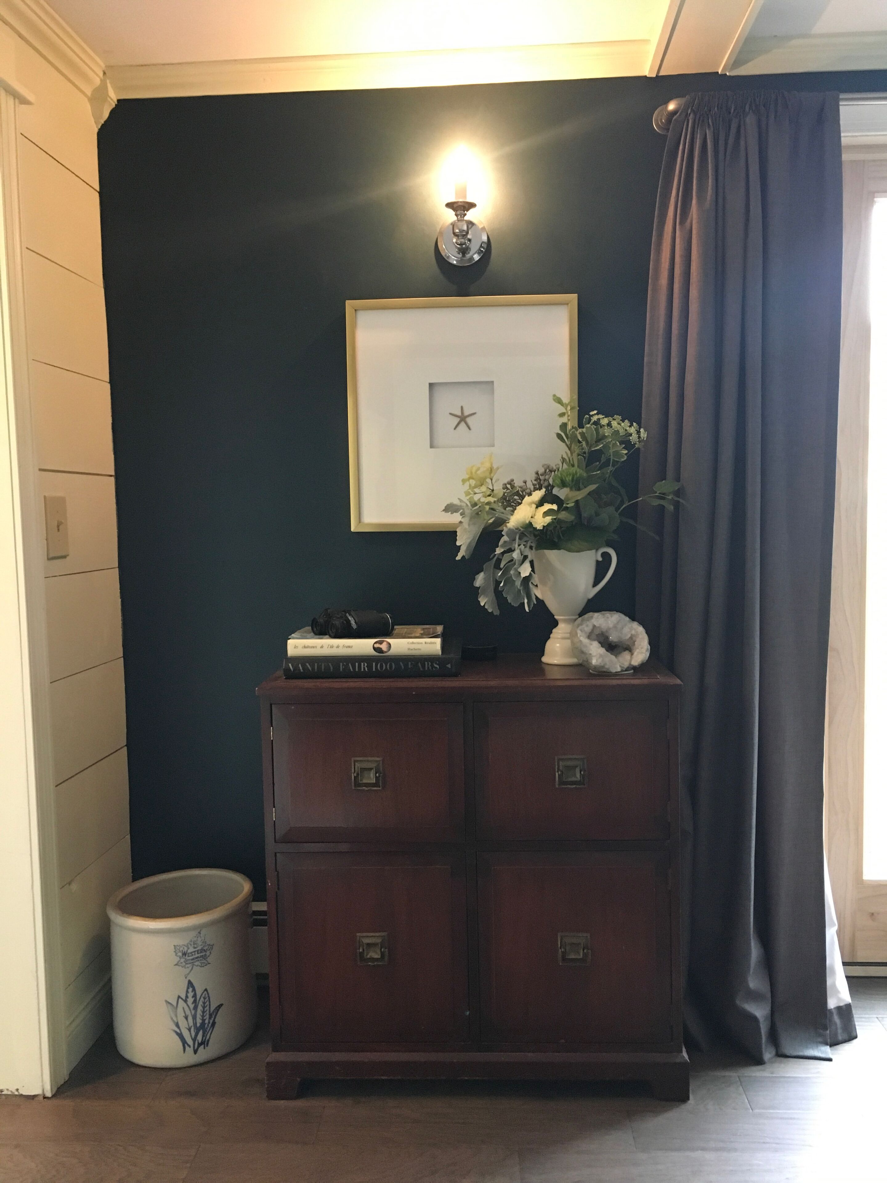 A dark blue wall with a framed picture of a starfish, a small potted plant, and a stack of books on a wooden cabinet.