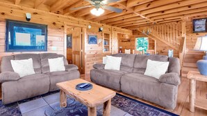 A cozy cabin interior with two sofas, a wooden coffee table, and a ceiling fan.