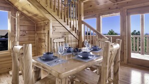A wooden cabin with a dining area, a staircase, and large windows.