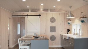 Una cocina moderna con una isla central, paredes de madera y una lámpara colgante.