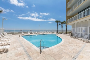 A pool area with lounge chairs and a view of the ocean.