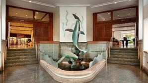Eine Lobby mit einer zentralen Springbrunnen-Skulptur, einer Treppe und Holzvertäfelung.