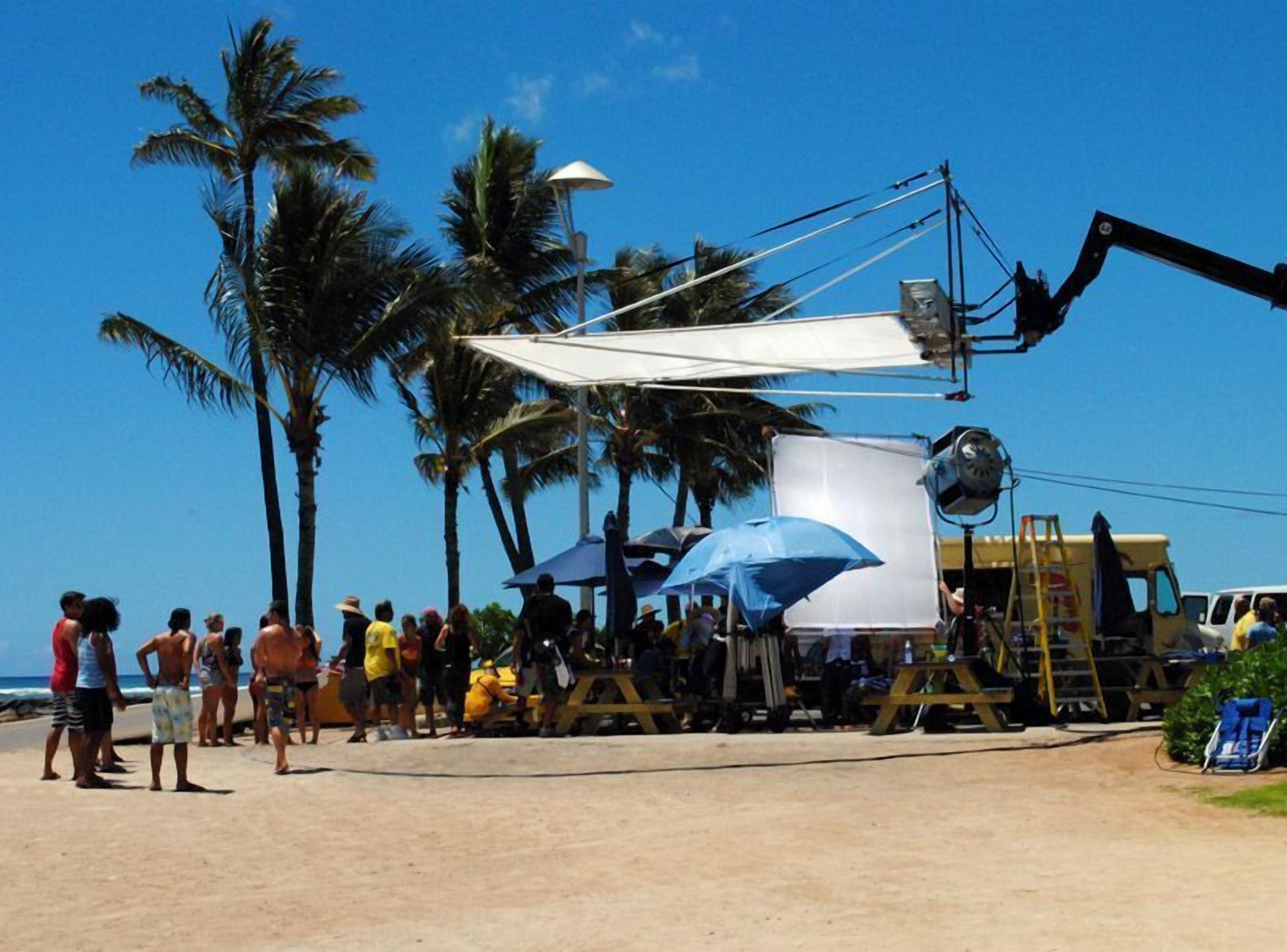 Escena de playa con palmeras, una multitud de gente y un vehículo de construcción.