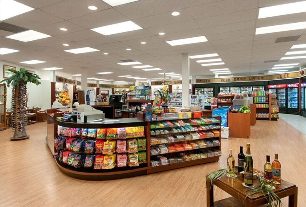 Interieur van een supermarkt met een centraal uitstalwandje van snacks, koelvakken en een kassa.