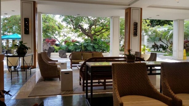 Eine großzügige Lobby mit einem großen Tisch und Stühlen, einem kleinen Tisch mit Pflanze und Blick auf üppiges Grün außerhalb.