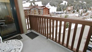 A balcony with a view of a snowy mountain landscape, a building with multiple windows, and a parking area.