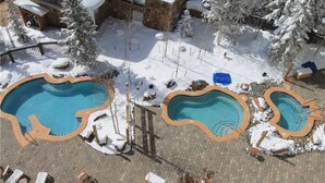A pool area with three pools, surrounded by snow-covered trees and a stone wall.
