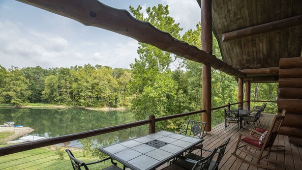 A wooden deck with a table and chairs overlooking a lake, surrounded by trees. - 3 acre Lake, Farm Animals Petting Zoo, Horses and Horseback Riding, Room to roam (Brownsburg)