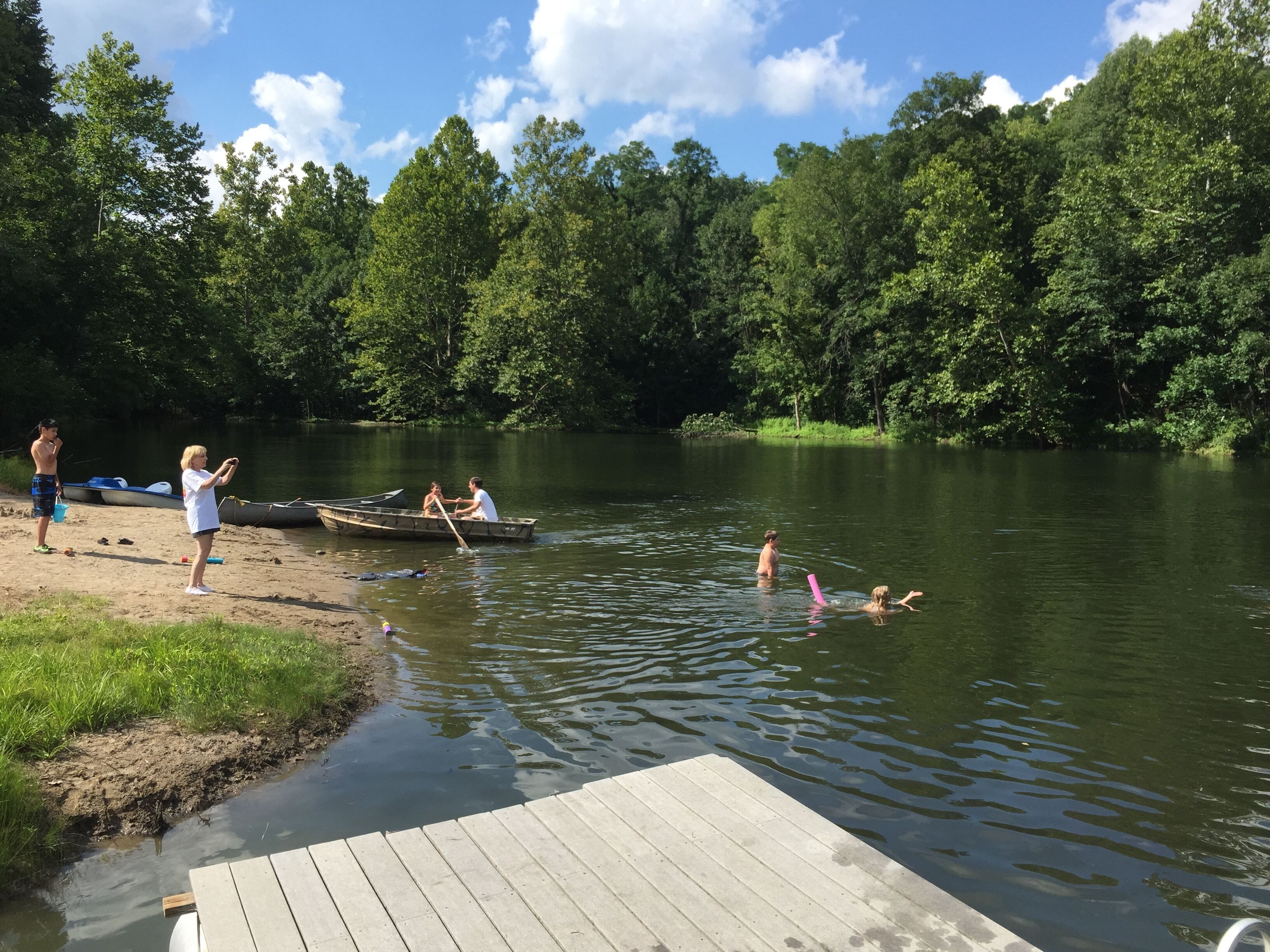 A lakeside scene with a dock, boats, and people engaging in water activities.