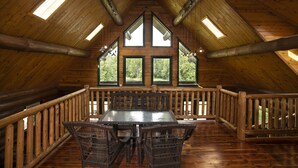 A spacious attic room with a wooden floor, a central table with chairs, and a balcony with a wooden railing. - 3 acre Lake, Farm Animals Petting Zoo, Horses and Horseback Riding, Room to roam (Brownsburg)