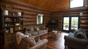 A cozy log cabin interior with a sofa, armchairs, a coffee table, and a TV. - 3 acre Lake, Farm Animals Petting Zoo, Horses and Horseback Riding, Room to roam (Brownsburg)