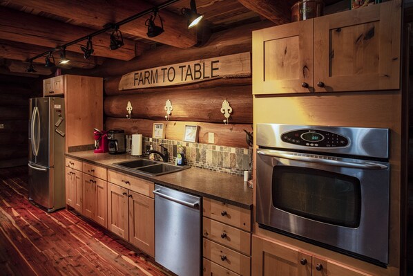 A kitchen with wooden cabinets, stainless steel appliances, a farmhouse-style sign, and a tiled backsplash.