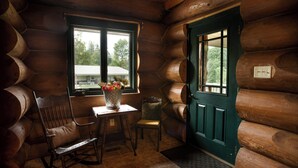 A log cabin interior with a wooden rocking chair, a small table with a vase of flowers, and a green door. - 3 acre Lake, Farm Animals Petting Zoo, Horses and Horseback Riding, Room to roam (Brownsburg)