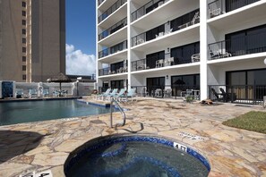 A hotel pool area with a stone deck, lounge chairs, and a hot tub.