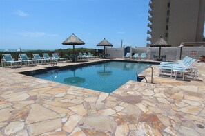 A pool area with stone flooring, lounge chairs, and thatched umbrellas. - Spacious Penthouse. Perfect for Families & Groups. Sleeps 12 (South Padre Island)
