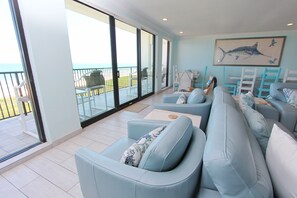 A modern living room with a large sliding glass door leading to a balcony. There are multiple seating areas with light blue sofas and white chairs. A large fish mural is on the wall. - Spacious Penthouse. Perfect for Families & Groups. Sleeps 12 (South Padre Island)