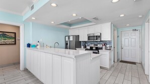 Una cocina moderna con armarios blancos, una isla central, electrodomésticos de acero inoxidable e iluminación empotrada en el techo.
