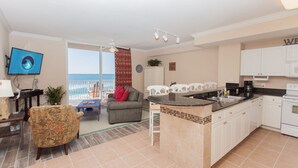 A modern kitchen with white cabinets, a black countertop, and a view of the ocean through a large window.