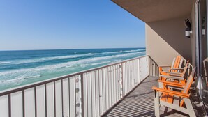 A balcony with a view of the ocean, featuring a railing and two orange chairs.