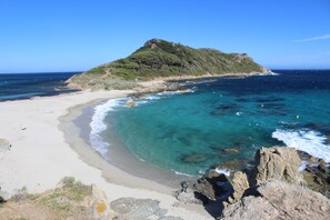 A beach with clear turquoise waters, a sandy shore, and a rocky outcrop.