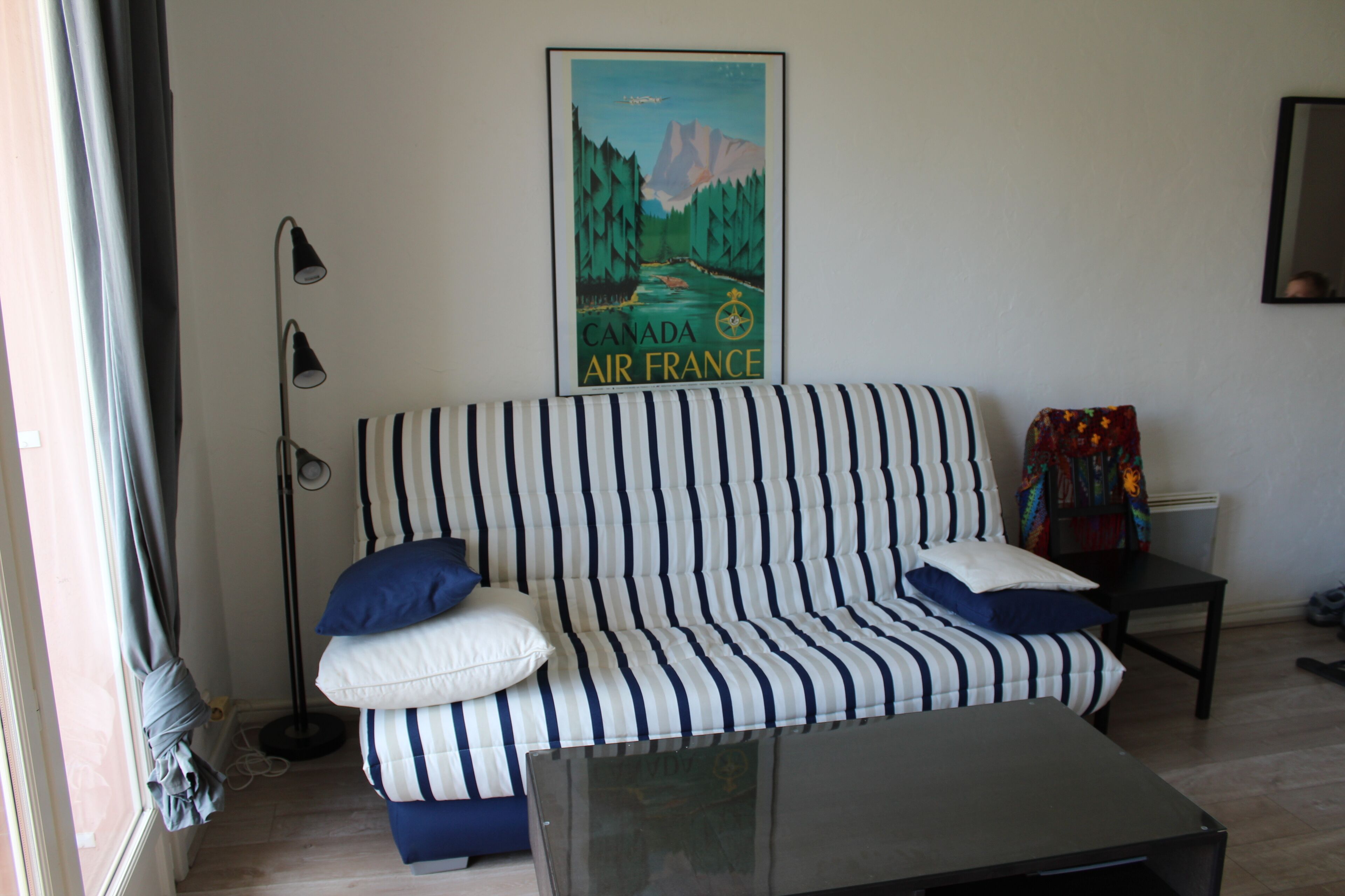 A striped sofa with pillows, a floor lamp, a poster on the wall, and a small table.