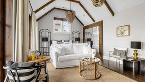 A cozy living room with a white sofa, a round coffee table, and a dining area with a striped chair. - Great for Large Groups | The Waltz (Charleston)