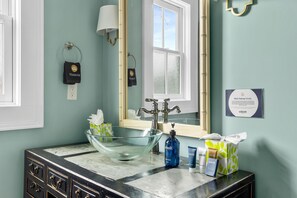 Ein Badezimmer mit einem Waschbecken aus Glas, einem Spiegel, einem Handtuchhalter und Toilettenartikeln.