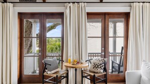 A room with a wooden door, two wicker chairs, a small round table with a bottle of orange juice, a cup, and a plate of fruit. - Great for Large Groups | The Waltz (Charleston)