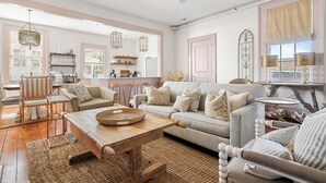 A cozy living room with a wooden coffee table, a sofa, and a chair. There is a kitchen area in the background with a dining table and chairs. - Great for Large Groups | The Waltz (Charleston)
