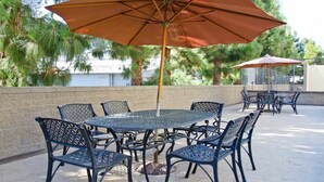 An outdoor patio with a round table and six chairs, surrounded by a low brick wall and palm trees.