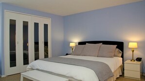 A bedroom with a bed, bedside lamps, a nightstand, a bench, and a wardrobe with mirrored doors.