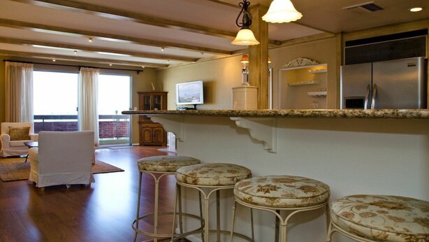 A spacious living room with a large window, a white sofa, and a dining area with a bar stool.